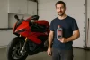 Homem segurando óleo ideal para motos esportivas ao lado de moto vermelha em oficina